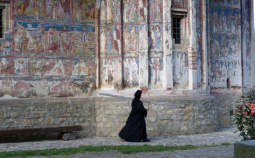Nun walking in front of the painted walls of Humor monastery
