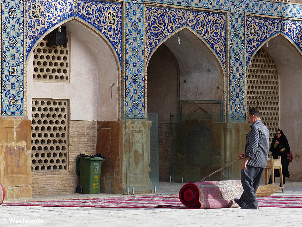 man rolling a carpet in a mosque courtyard