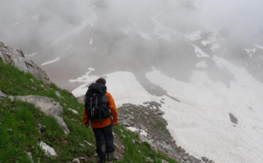 Hiker in an orange jacket on a foggy mountain path