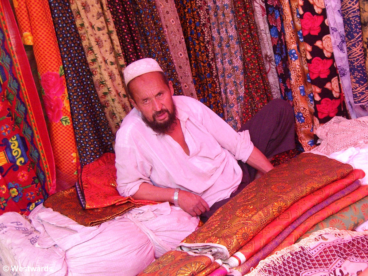 Uighur vendor leaning on bales of colourful cloth